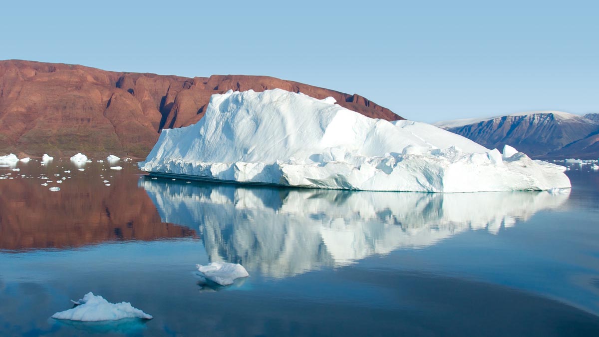 Blick auf eine Eisscholle, die vor einer kargen Insel im artkischen Meer treibt