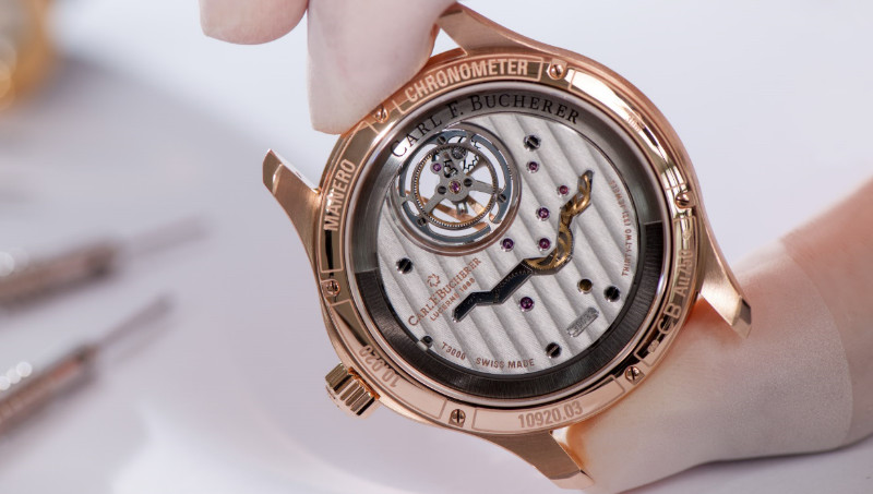 Close-up of a Carl F. Bucherer chronometer held by the gloved fingers of a watchmaker