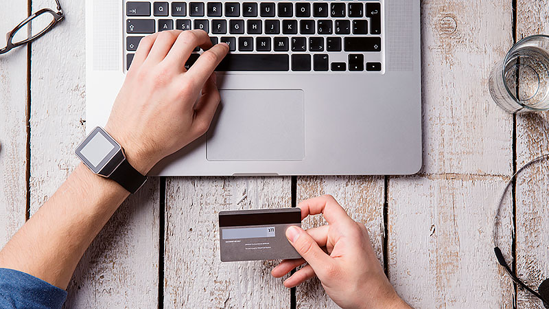 L'e-commerce comme thème d'investissement: on peut voir les mains d'une personne qui est en train de payer avec ordinateur portable. Une main tient la carte de crédit, l'autre tape sur le clavier.