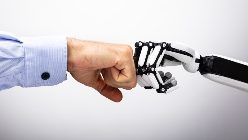 La robotique comme thème d'investissement, illustré par le poing serré entre une main humaine et une main de robot.
