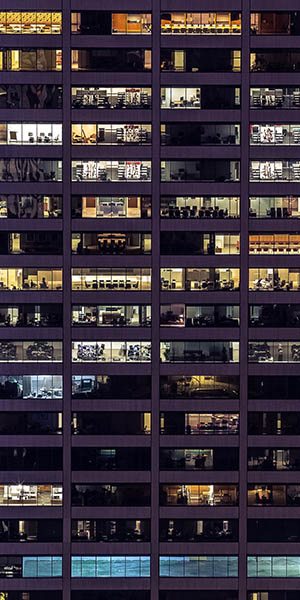 The facade of a skyscraper at night, with countless windows. It illustrates increasing urbanization and population density.