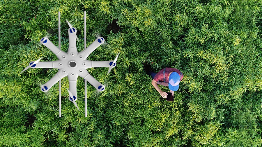 Smart farming as an investment theme: On the e-farm, a drone hovers over green plants. A farmer with a smartphone controls it.